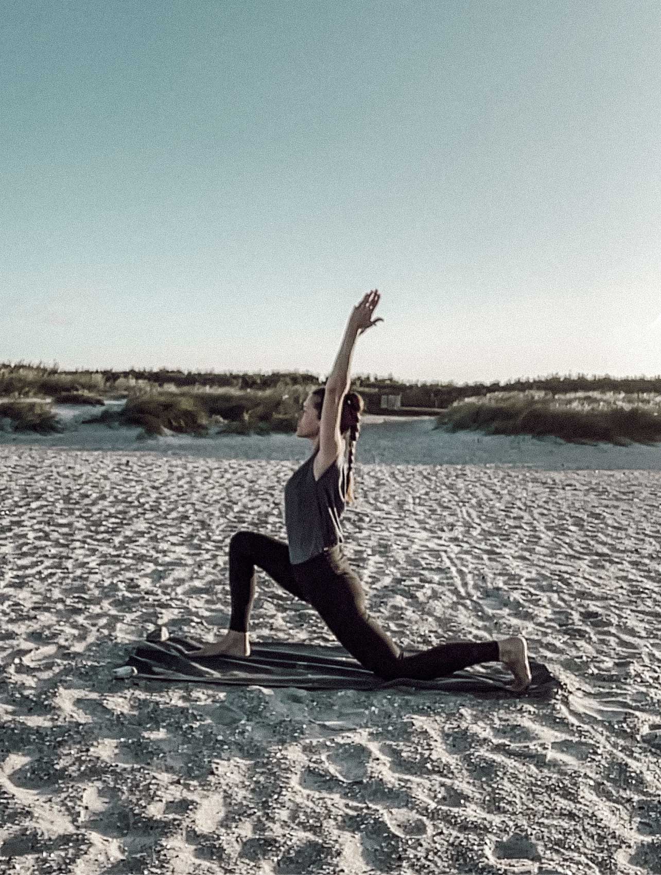 Katja in einer Yogapose Ausfallschritt mit hinterem Knie am Boden, Arme gestreckt nach oben in einer Dünenlandschaft